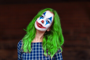 Close-up portrait of a greenhaired girl in chekered dress with joker makeup on a blurry background. - obrazy, fototapety, plakaty