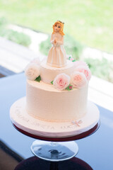 A birthday cake with flowers and a doll on it, standing on the table