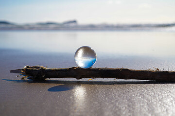 Photography Crystal Photo Ball showing upside down reflection of sky beach and waves balanced on rocks on sandy beach.