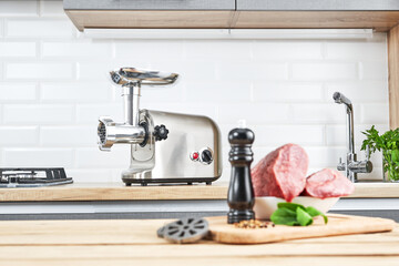 Meat grinder with fresh meat on a wooden table in kitchen interior