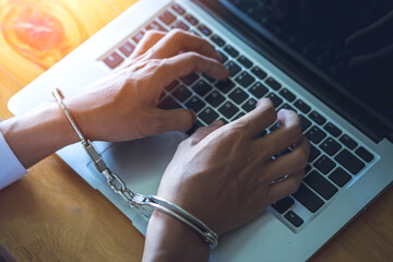 Hands of hacker with handcuffs above notebook keyboard, punishment for cybercrime, business concept.