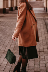 Young woman with cropped face in the orange knitted sweater and brown coat, outdoor portrait in daylight. Cozy autumn.