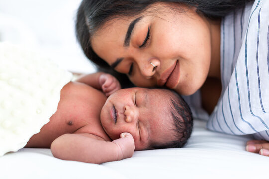 African American Mum Hugging And Kissing Her Newborn Baby On White Bed. Close Up Of Infant With Young Mother