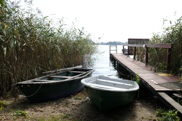 Fototapeta na wymiar Landscape with wooden pier and boats on the lake shore among the reeds.