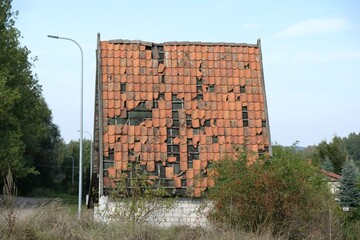 A house with a high sloping red tiled roof. Destroyed roof with falling tiles.