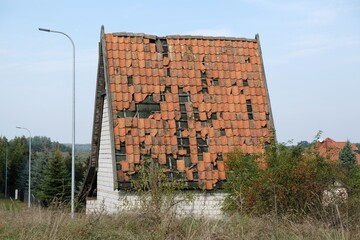A house with a high sloping red tiled roof. Destroyed roof with falling tiles.
