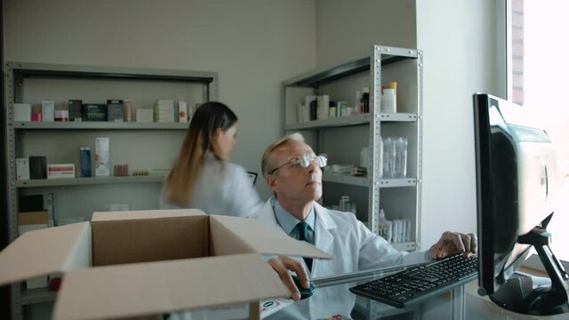 Time-lapse shot of two pharmacy employees, preparing order for client. Mature man and young woman manually packing box with medicine products for delivering. City Drug store with big assortment.