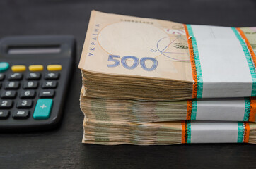 stacks of hryvnia and a calculator on a black wooden background. Ukrainian money. Financial concept. Lots of banknotes. Close-up.