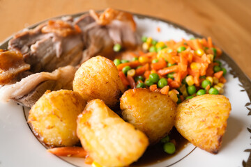 Golden crispy roast potatoes as part of a home made roast dinner of pork and vegetables.