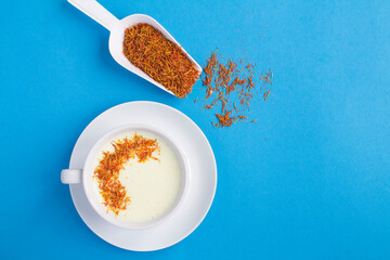 Top view of saffron latte or saffron moon milk in the white cup on the blue background with copy space
