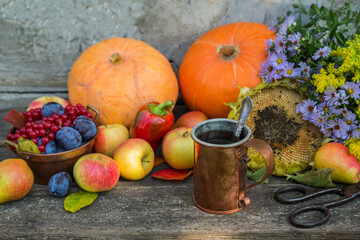 Copper mug with tea against the background of the autumn harvest of pumpkins, apples, plums, pears and viburnum on a wooden table. Vintage rustic style