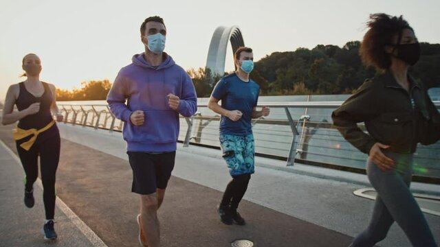 Quarantine and sport. Group of diverse millennial people jogging early in morning, wearing protective masks, slow motion