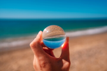 A photo of the ocean through a circular crystal ball turning the picture in the ball upside down. The picture in the ball is in focus and the background is out of focus.