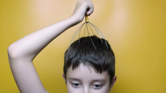 A caucasian boy enjoy head scalp massage by anti stress acupuncture metal octopus tool, equipment, she closes her eyes with pleasure, yellow background, close up view