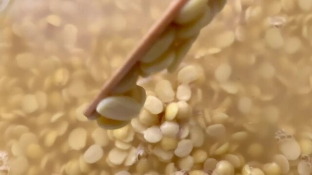 Stirring a pot of soaked split pigeon peas with a wooden ladle and dropping them back into the water