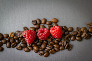Kaffeebohnen mit drei Himbeeren auf grauem Hintergrund