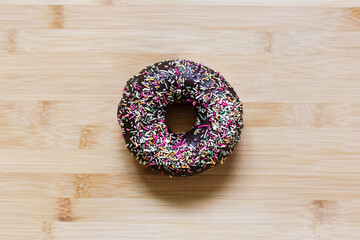 Top view of chocolate donut with sprinkles on wooden table.