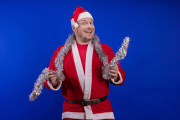 Male actor in a suit and hat of Santa Claus with a silver tinsel garland dancing and posing on a...