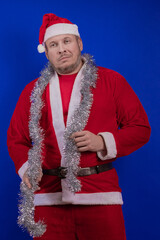 Male actor in a suit and hat of Santa Claus with a silver tinsel garland dancing and posing on a...