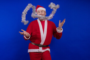 Male actor in a suit and hat of Santa Claus with a silver tinsel garland dancing and posing on a...
