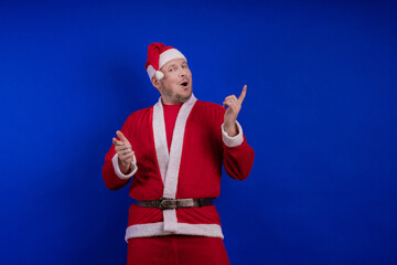 Male actor in costume and hat of Santa Claus posing on a blue background.