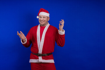 Male actor in costume and hat of Santa Claus posing on a blue background.
