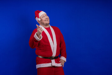 Male actor in costume and hat of Santa Claus posing on a blue background.