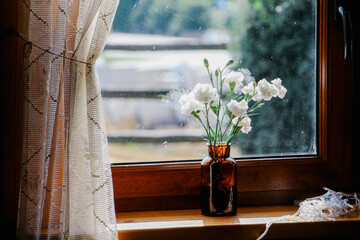 small vase with white flowers on the windowsill close up