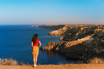 Rear view of traveler woman standing on cliff edge in front of amazing seascape. Freedom, travel and vacation concept.
