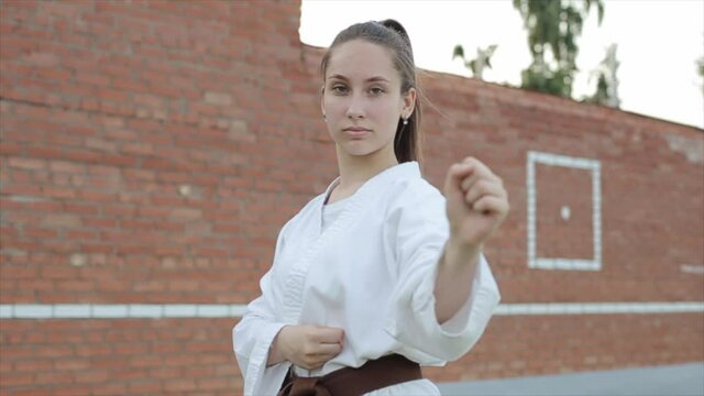 Portrait of a young girl in a white kimono who stands in a basic karate stance against the background of a brick wall. Slow motion. The camera moves from side to side