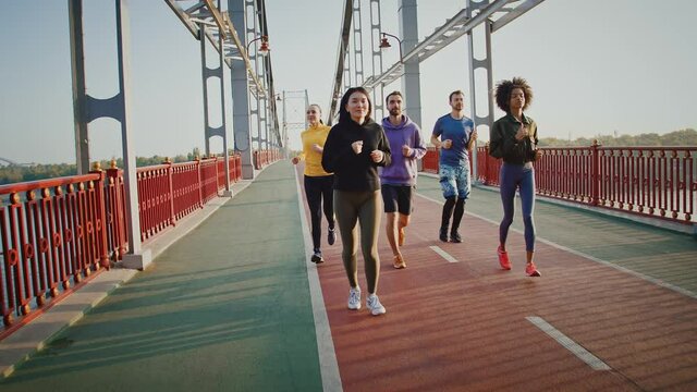 Sporty friends practicing morning jog on sports bridge in city, slow motion