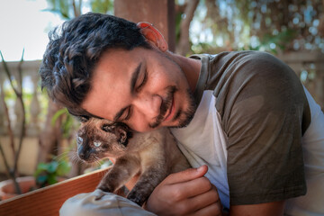 primer plano. Hombre joven abraza a un gato siames en el jardin