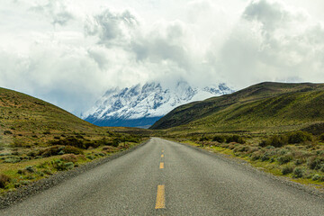 bela paisagem de estrada asfaltada vazia, com campo nas laterais e vai em direção a grandes montanhas cobertas de gelo