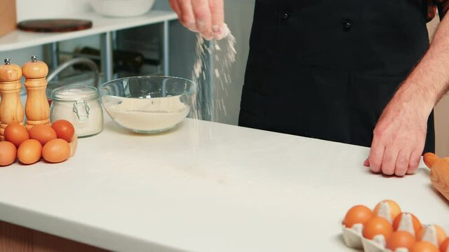 Baker spreading cookies ingredient on kitchen table top. Retired senior chef with bonete and apron, in kitchen uniform sprinkling sieving sifting ingredients by hand baking homemade pizza and bread