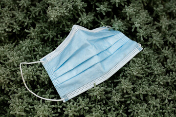 Waste during COVID-19. Discarded to single-use coronavirus masks. Environmental pollution, on green plants