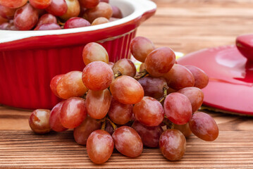 Ceramic pot with red grapes on wooden table.