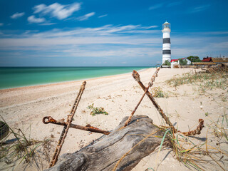 wide angle view to the old lighthouse through two old anchors in summer day on the beach under blue sky with copy space