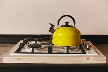 Yellow steel kettle on the gas hob on the wooden table. Modern yellow kettle on the stainless steel...