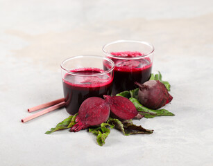 Beetroot drink cocktail in a glass with a bamboo straw on a light gray background