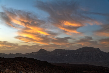 Obraz premium Beautiful orange clouds in the sky over the caldera in the Teide region on the island of Tenerife in the early morning before sunrise. The ground resembles a lunar landscape.