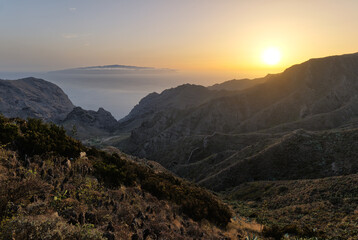 View through a valley of the Teno Mountains on the island of Tenerife at sunset. In the distance the Atlantic Ocean and on the horizon the neighboring island of La Gomera surrounded by clouds.