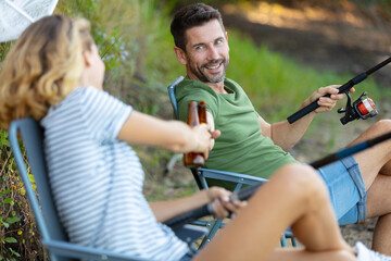 Obraz premium woman and man having a beer while fishing lakeside