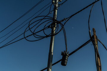power lines, electric poles with black straight and twisted wires and small transformer bank. Backdrop blue gradient sky with moon