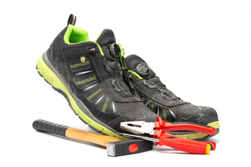 Pair of black work shoes with with green lining along with a hammer with wooden handle, a red pliers and a red Phillips screwdriver. With a white background.