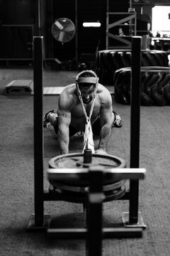 A muscular man pulls a weight sled with his head
