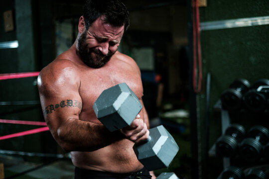 Muscular man straining to lift heavy dumbbell