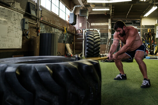 An muscular man hits a large tire with a sledgehammer
