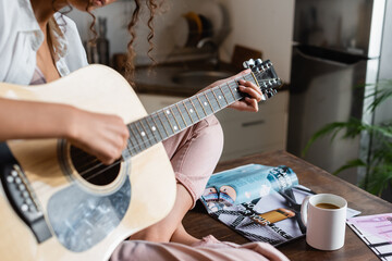 cropped view of young woman playing acoustic guitar at home