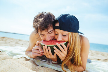 Teenage couple biting a watermelon on the beach.