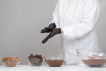 Chocolatier in white uniform step-by-step making hand-crafted dark chocolate truffles, preparing delicious handmade chocolate candies, rolling truffle between palms forming round shape, confectionery
